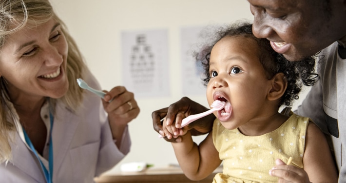 parent and doctor showing young child how to brush teeth